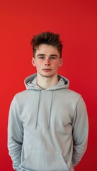 Obraz premium Casual Young Man in Light Grey Hoodie Against Vivid Red Background for Lifestyle Design