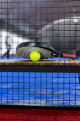 Padel racket resting on a wooden bench with a bright yellow or green ball in a well-lit indoor padel court during a match