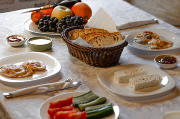 A cozy breakfast spread featuring a mix of fresh fruits, sliced vegetables, bread, cheese, and pancakes. The table is set with a rustic wicker basket for bread, creating a warm atmosphere 