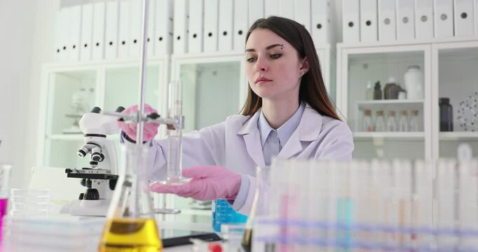 Woman scientist in white robe adjusts burette at workplace in modern laboratory. Focused female technician prepares for conducting research