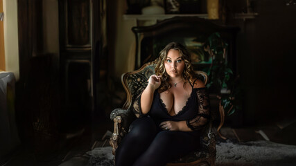 Plus-size model with bright makeup in black bodysuit and curvy body in a sensual pose on dark background. © angelo lano