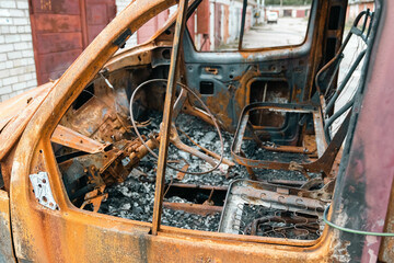 Rusty burnt out car in an abandoned backyard showing steering wheel and seats