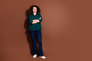 Confident young woman with curly hair standing against brown background in casual green shirt and...