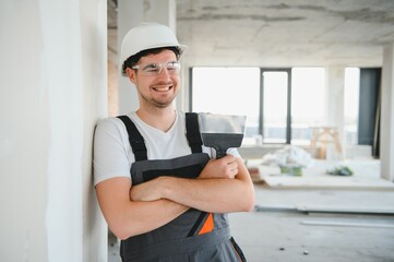 Worker in uniform plastering wall with putty knife indoors