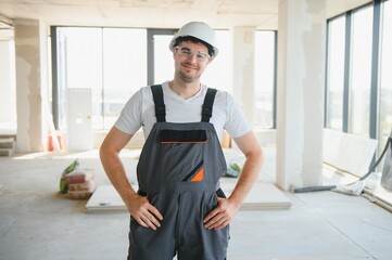 Handsome young male builder in hard hat, while working at construction site.