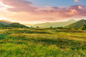 scenic landscape of green and golden sunset field in a valley between mountains with beautiful...