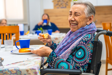 Happy elder woman with disability eating breakfast at geriatrics