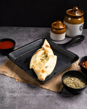 A cheese fatayer displayed on a black pan with a side of spices and sauces