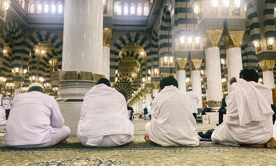 Four people wearing white robes sitting inside the Al Masjid an Nabawi mosque in medina, saudi arabia