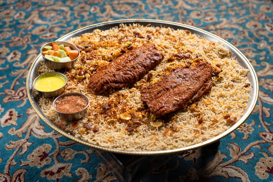 Fried fish mandi platter with a side of vegetables and sauces displayed in a large stainless steel platter