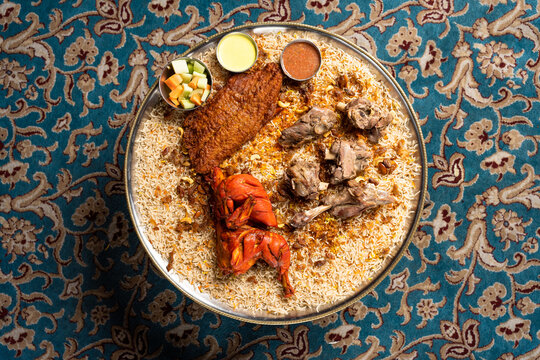 Flat lay of chicken mandi Arabian dish with a side of vegetables and sauces