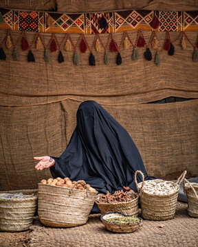 Woman wearing a burka sitting on the ground in front of baskets of nuts