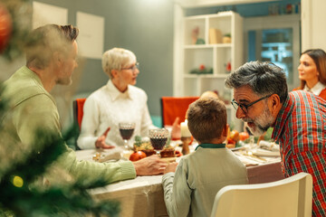 Obraz premium Grandfather whispering to grandson during christmas dinner with family