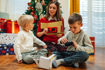 Two little brothers unpacking christmas presents with their mother