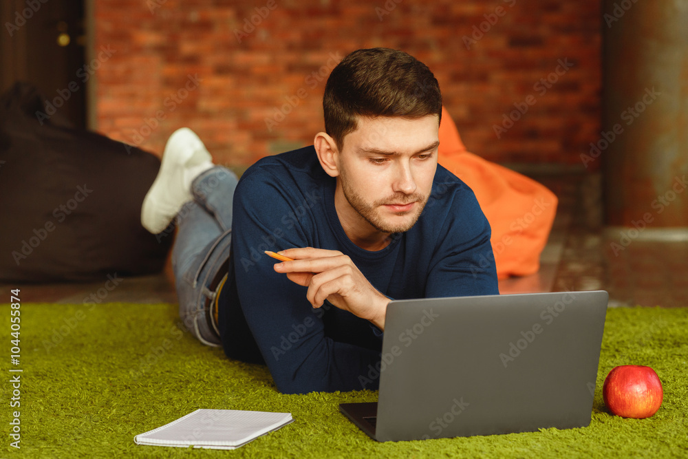 Aufkleber Millennial Guy Using Laptop Working Online And Creating Business Startup Lying On Floor At Home. Selective Focus