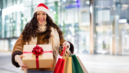 Excited woman holding shopping bags and Christmas present in her hands, prepare for winter holidays, enjoy Xmas sales and gifts, panorama with copy space