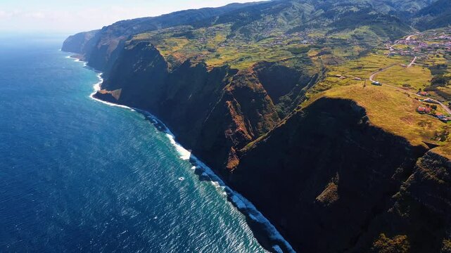 Town located in the valley on top of the picturesque mountain. Drone footage above the waterscape of the Atlantic Ocean. Madeira, Portugal from top view.