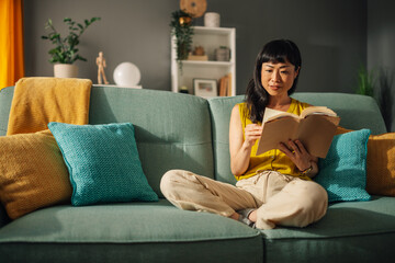 Obraz premium Relaxed asian woman reading a book on a stylish couch