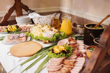 Rustic wedding table. Homemade sliced meats, assorted cheese board and a jar of pickled cucumbers. Traditional banquet setup in Eastern Europe, offering authentic regional cuisine.