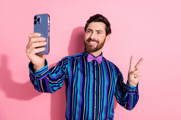 Photo of attractive funny nice man wear trendy clothes hold gadget make video selfie v-sign isolated on pink color background