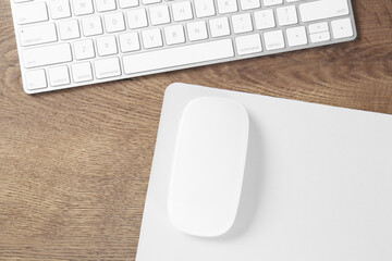 Computer mouse with mousepad and keyboard on wooden table, flat lay