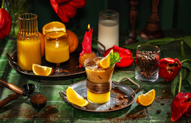 Iced coffee with orange juice being poured into glass with milk and flowers in background