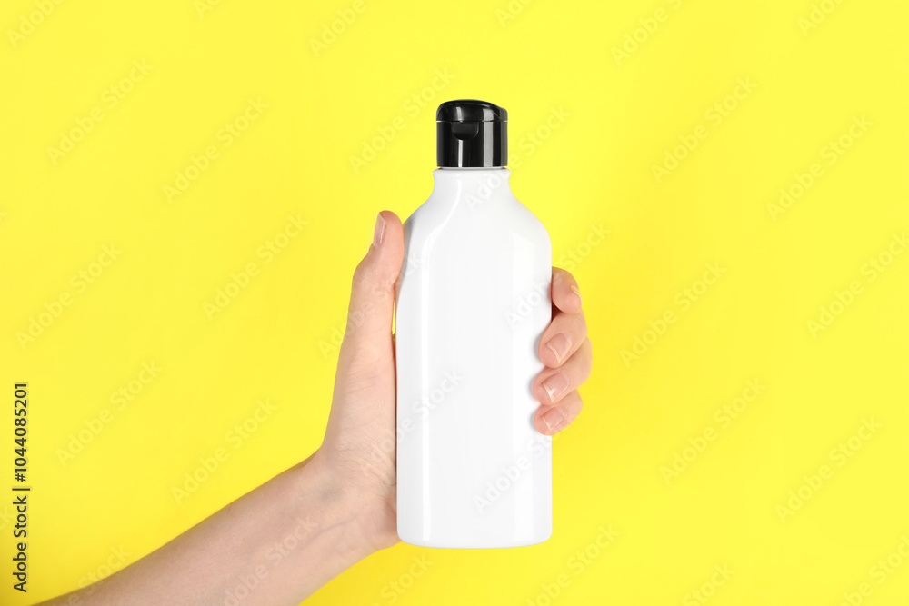 Poster Woman with shampoo bottle on yellow background, closeup