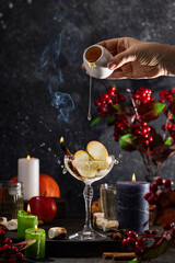 Bartender pouring honey into sparkling cocktail with apple slices and cinnamon stick