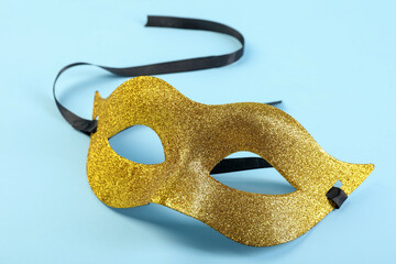 One golden carnival mask on light blue background, closeup