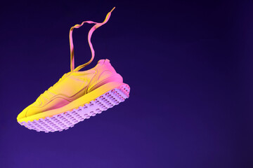 Stylish sneaker in air against dark purple background in neon lights, space for text