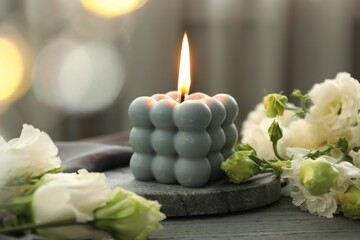 Burning bubble candle and beautiful flowers on grey wooden table, closeup