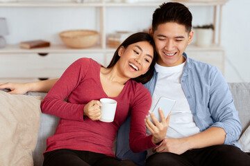 Spending Time Together. Asian family using smart phone sitting on couch at home, empty space