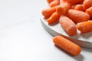 Frozen baby carrots on white table, closeup. Space for text