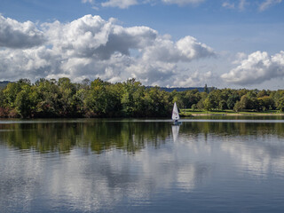 A sailboat is sailing on a lake with a cloudy sky in the background
