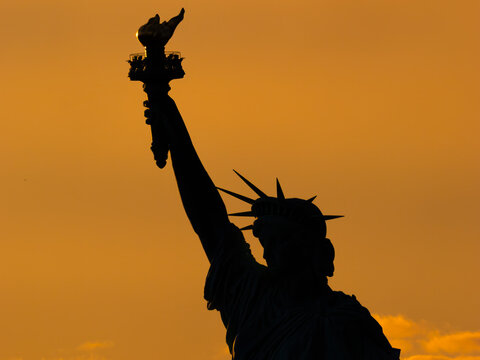 Stunning silhouette of the upper Statue of Liberty suring sunset in New York Harbor, within New York City. NY, USA - Powered by Adobe