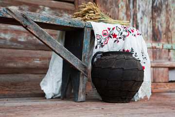 Vintage clay pot with an embroidered towel and a bouquet of wheat ears against an old wooden wall....