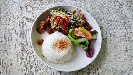 Crispy Fried Pork with Steamed Rice and Fresh Sambal Matah, Served with Salad Garnish on a Rustic Wooden Table