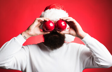 Santa man with Christmas balls. Bearded man in Santa hat covering eyes with New Year's toy balls....