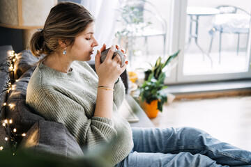 Pregnant woman enjoying a relaxing moment with a warm cup of tea, focusing on prenatal health and...