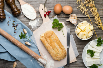 Cheese burek on Wooden Board with Rustic Cooking Ingredients. Puff Pastry and Fresh Ingredients Ready for Cooking, Rustic Style. Balkan national dish.