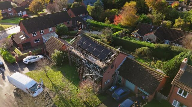 Aerial shot of new solar panel installation on family home. Drone ascends and backs away to reveal housing estate surrounded by countryside