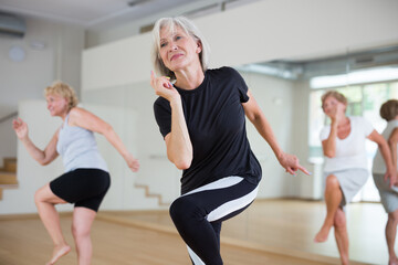 Positive aged woman practicing vigorous dance movements in group dance class .