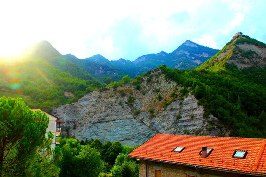 Impressive view from Acquasanta Terme at a massive rocky ridge with rich thickets and green vegetation, its imposing cusps standing tall like sawteeth, dominating the underlying homes with orange roof