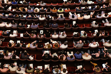 Theater audience with a view from above with almost all the seats occupied, arranged in rows.