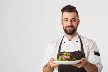 Chef is holding a plate of fresh food, smiling slightly as he presents his culinary creation