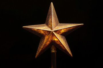 Golden glitter Christmas star ornament glowing warmly against a black background