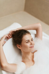 Obraz premium Relaxed European woman enjoying a bubble bath in a bright bathroom, displaying a serene expression while soaking in wellness and tranquility.