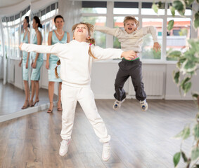 Cheerful preteen girl captured in air while jumping during lively dance lesson with boy classmate...
