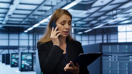 IT specialist looking over data center maintenance checklist, talking on phone in server farm....