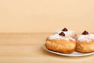 Plate with tasty donuts for Hanukkah celebration on wooden table against color background